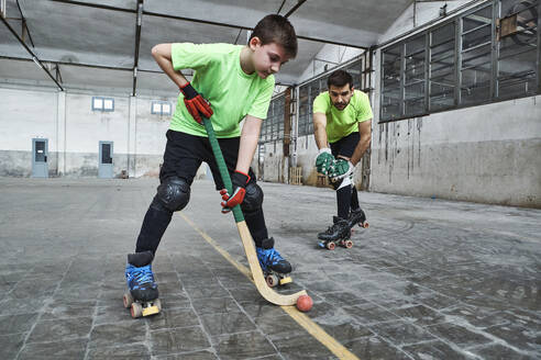 Boy practicing roller hockey with father on court - VEGF02844