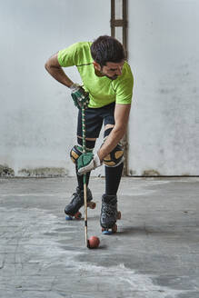 Mature male athlete practicing roller hockey against wall at court - VEGF02846