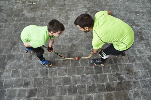 Boy in face off with father while playing roller hockey on court - VEGF02851