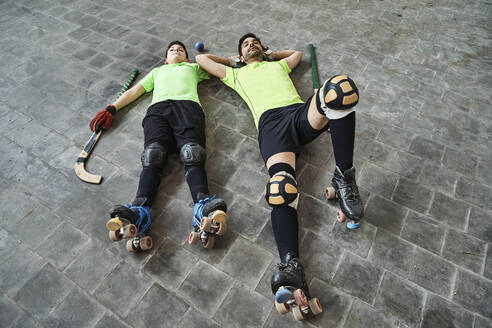 Tired father and son lying on floor after practicing roller hockey at court - VEGF02854