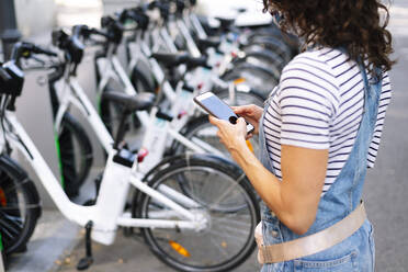 Frau steht in der Nähe eines Fahrradständers und benutzt ein Smartphone in der Stadt - JCMF01193