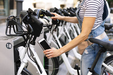 Midsection of woman scanning QR code on bicycle parking station - JCMF01195
