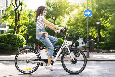 Woman riding electric bicycle on street during COVID-19 - JCMF01200