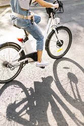 Tiefschnitt einer Frau, die an einem sonnigen Tag auf der Straße Fahrrad fährt - JCMF01201