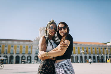 Sich umarmende Frauen am Praca Do Comercio bei klarem Himmel, Lissabon, Portugal - DCRF00695