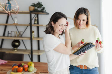 Freunde lernen über Ernährung, während sie zu Hause eine Erdbeere und ein digitales Tablet in der Hand halten - MRRF00316