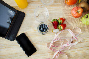 Digital tablet and mobile phone kept with fruit and measurement tape on table at home - MRRF00328