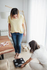 Friends measuring weight with weight scale at home - MRRF00332