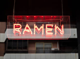 Illuminated signboard with restaurant name Ramen symbolizing traditional Japanese dish hanging outdoors - ADSF12211