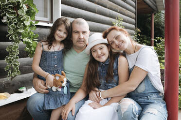 Happy family sitting on porch of house - EYAF01269