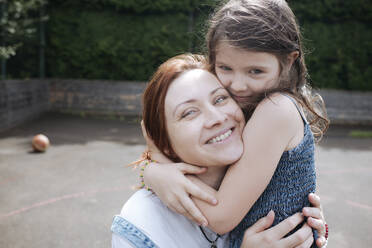 Mädchen umarmt lächelnde Mutter am Basketballplatz im Hinterhof - EYAF01276