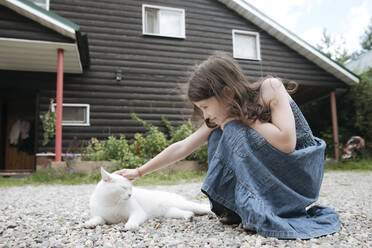 Kleines Mädchen streichelt Katze im Vorgarten des Hauses - EYAF01280