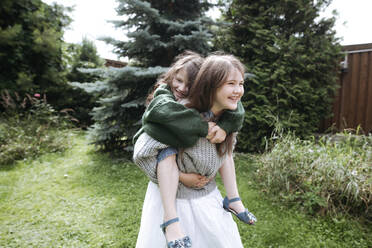 Girl giving piggyback ride sister in back yard - EYAF01283