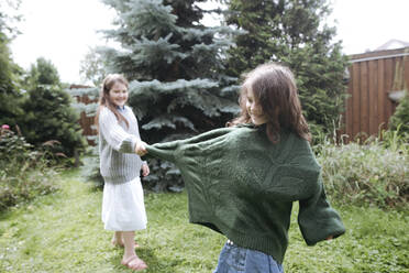 Playful girl pulling sister's sweater sleeve at back yard - EYAF01284