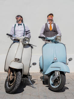 Verträumte Hipster mittleren Alters in modischer Kleidung mit Retro-Motorrädern an der Wand lehnend an einem sonnigen Tag - ADSF12217