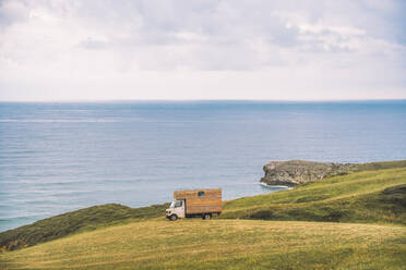 Goldene Feld auf dem Hügel und kleine Ladung LKW mit blauem Meer und bewölktem Himmel auf dem Hintergrund in Comillas Cantabria in Spanien - ADSF12234