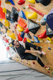 From bellow strong male athlete in sportswear climbing on colorful wall during workout in modern guy - ADSF12324