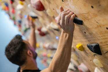 Side view of blurred anonymous strong male athlete in sportswear climbing on colorful wall during workout in modern guy - ADSF12327