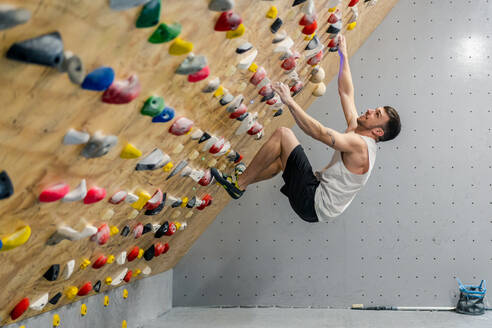 From bellow side view of strong male athlete in sportswear climbing on colorful wall during workout in modern guy - ADSF12328