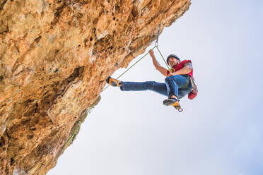 Von unten gesichtsloser männlicher Alpinist beim Klettern am steilen Felsen an einem Sommertag - ADSF12338