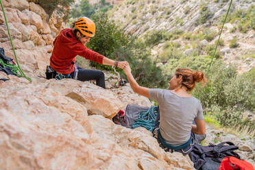 Von oben Rückenansicht von sportlichen jungen Bergsteigerinnen, die sich an einem sonnigen Tag auf einem Felsen ausruhen und die Fäuste zusammenschlagen - ADSF12343