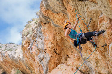 Furchtlose junge Bergsteigerin beim Aufstieg auf einen Felsen in den Bergen im Sommer - ADSF12348