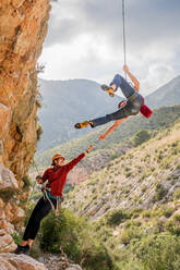 Aktiver junger Bergsteiger, der einen Freund beim Abstieg vom Felsen unterstützt, an einem Sommertag - ADSF12351