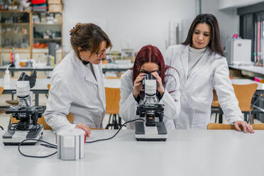 Female scientist inspecting tissue sample with contemporary microscope near coworkers while working in modern lab - ADSF12411