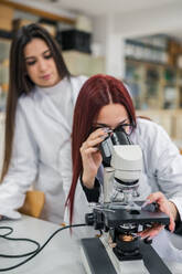 Woman using microscope near colleagues in laboratory - ADSF12413