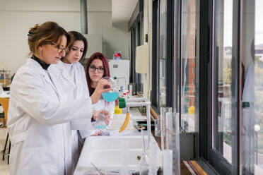 Female students watching mentor conducting experiment in lab - ADSF12425
