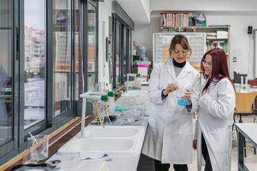 Positive mature woman showing chemical experiment to happy female student while working in modern laboratory in university - ADSF12436