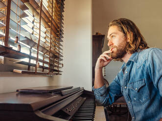 Thoughtful male playing synthesizer at home - ADSF12443