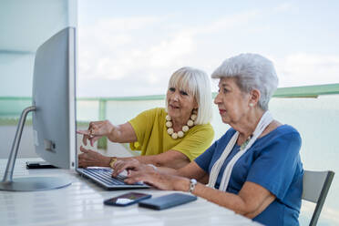 Stilvolle alte Freunde sitzen am Tisch mit Computer auf dem Balkon eines Resorts - ADSF12459