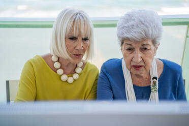 Stilvolle alte Freunde sitzen am Tisch mit Computer auf dem Balkon eines Resorts - ADSF12462