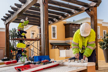 Gruppe männlicher Techniker in Uniform bei der Arbeit mit alternativen Solarmodulen und der Vorbereitung für die Installation in der Nähe eines Wohnhauses - ADSF12484