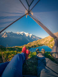 Relaxed tourists lying in tent in snowy mountains in sunlight - ADSF12501