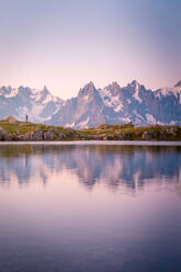 Lonely tourist on hilly shore reflecting in crystal lake in snowy mountains in sunlight - ADSF12509