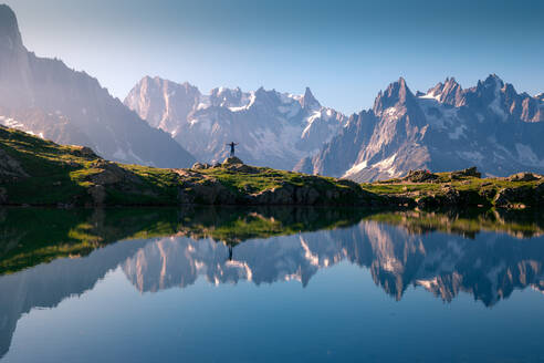 Einsamer Tourist am hügeligen Ufer, der sich in einem kristallklaren See in verschneiten Bergen im Sonnenlicht spiegelt - ADSF12511