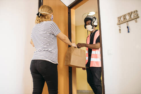 Woman taking paper bag from delivery man with protective mask - GMLF00502