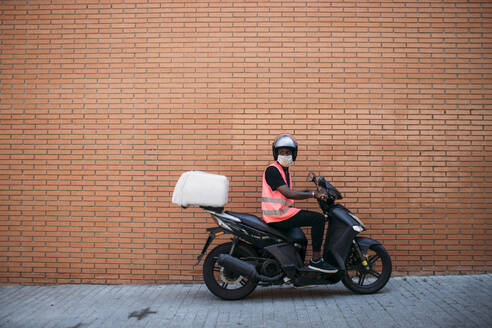 Delivery man on motorbike with protective mask delivering food - GMLF00503