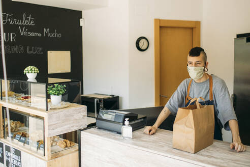 Young man with protective mask in cafe waiting for delivery man - GMLF00505
