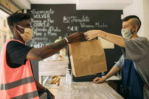 Delivery man with protective mask picking up an order from restaurant - GMLF00506