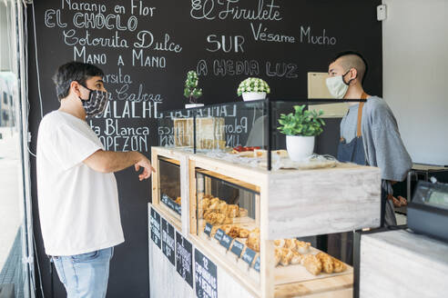 Waiter and customer with protective masks at the counter in a cafe - GMLF00511