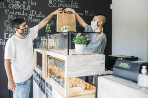 Kellner und Kunde mit Schutzmasken am Tresen eines Cafés - GMLF00512