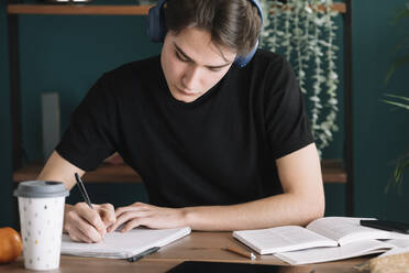 Mann schreibt in ein Buch, während er zu Hause über Kopfhörer Musik hört - ALBF01388