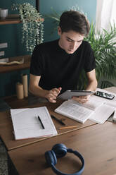 Junger Mann benutzt ein digitales Tablet, während er am Tisch sitzt und Hausaufgaben macht - ALBF01391