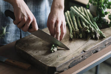 Hands of man cutting fresh asparagus on board in kitchen - ALBF01401