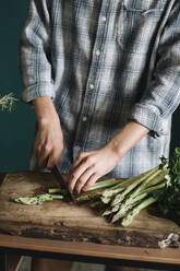 Midsection of man cutting fresh asparagus on board in kitchen - ALBF01402