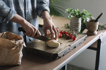 Hände eines Mannes, der frisches, hausgemachtes Brot auf einem Brett in der Küche schneidet - ALBF01403