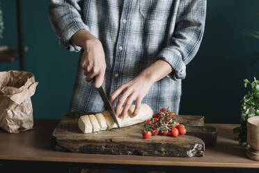 Mittelteil eines Mannes, der frisches selbstgebackenes Brot mit Kirschtomaten auf einem Brett in der Küche schneidet - ALBF01404